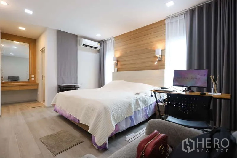 独立式住宅 出租或出售在Prawet, Bangkok - 主卧配木质特色墙、书桌角和带窗帘的大窗。
