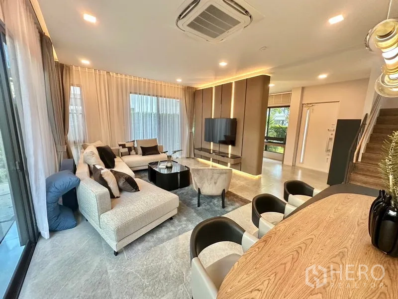 Detached House for rent in Samut Prakan - Open-plan living area with L-shaped sofa, TV wall and a breakfast bar.