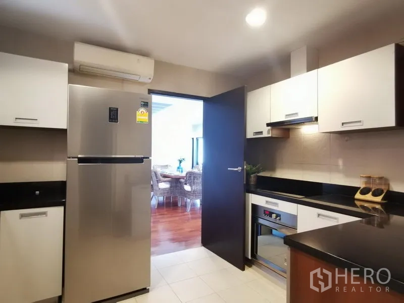Condominium for rent or sale in Khlong Toei, Bangkok - Separate kitchen with white cabinetry, black countertops, stainless-steel fridge, and built-in oven.