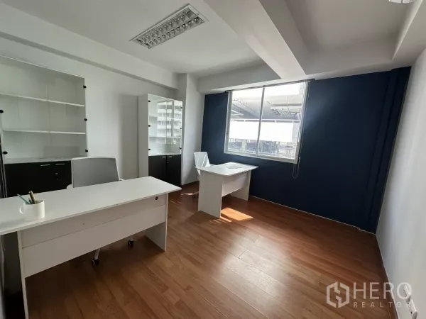 办公空间 出租在Watthana, Bangkok - 私密办公室，两张白色书桌，大窗户与展示柜，深蓝色背景墙。