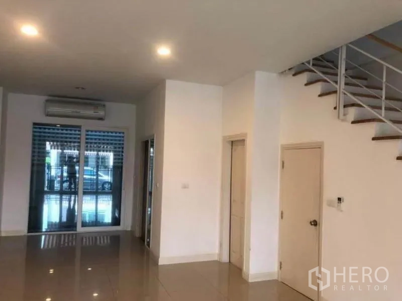 联排别墅 出租在Wang Thonglang, Bangkok - 一层客厅采光充足，亮面地砖、嵌灯、推拉玻璃门与楼梯。