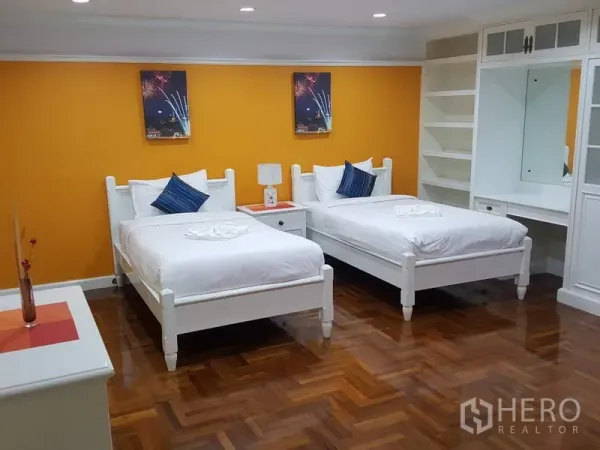 公寓 出租在Watthana, Bangkok - 双床卧室，橙色背景墙，白色床架，内置衣柜与开放式搁架。