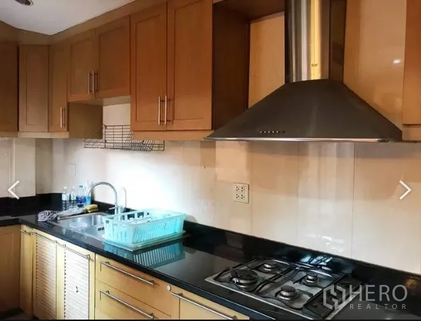 Detached House for sale in Saphan Sung, Bangkok - Fitted kitchen with granite countertop, gas hob, stainless range hood and wooden cabinets.