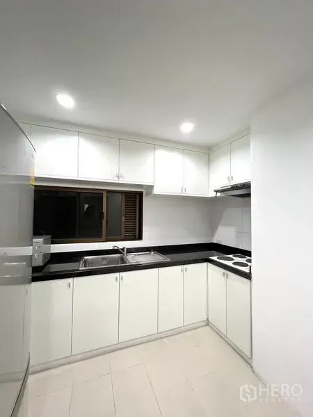 公寓 出租在Watthana, Bangkok - U形白色厨房，黑色台面、双水槽与上柜，照明充足。