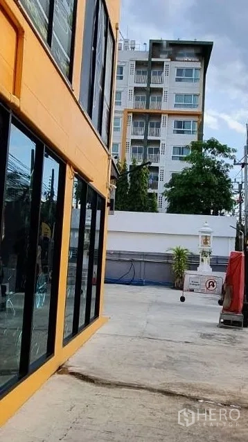 Home Office for rent in Phra Khanong, Bangkok - Paved side yard between the building and boundary wall with a small spirit house and plants.