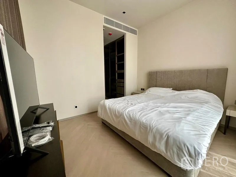 Condominium for rent - Cozy bedroom with upholstered bed, white bedding, TV console, and doorway leading to a walk-in closet.
