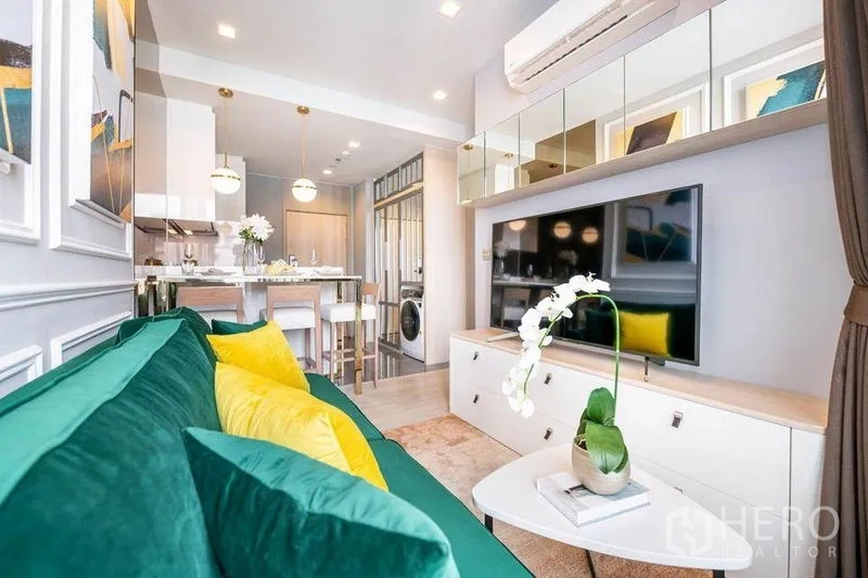 Condominium for rent or sale in Watthana, Bangkok - Living area facing TV wall and storage unit with balcony doors and dining zone beyond.