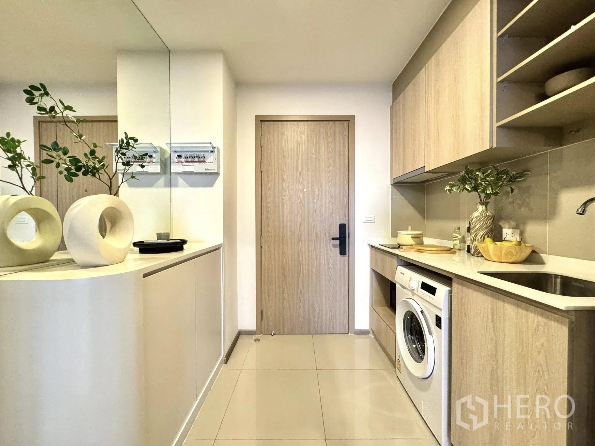 Condominium for rent in Watthana, Bangkok - Galley kitchen with light-wood cabinets, countertop, sink, and washing machine.