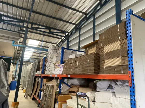 Factory for sale in Khlong Luang, Pathum Thani - Warehouse aisle with metal shelving stacked with cartons and materials.