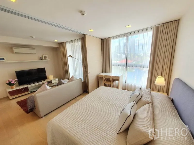 Condominium for rent in Watthana, Bangkok - Bright open-plan condo with king bed, sofa, TV and a desk beside large windows with city view.