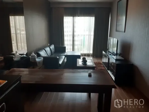 公寓 出租在Bangkok - 客厅配L形真皮沙发、电视柜、木地板以及落地窗与纱帘。