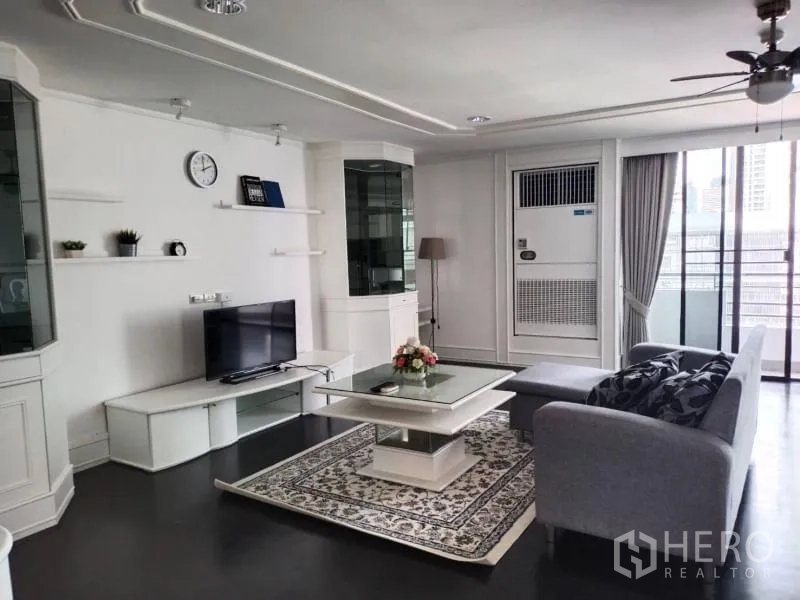 Condominium for rent in Sathon, Bangkok - Living room with TV console, wall shelves, L-shaped sofa, rug, and access to the balcony.