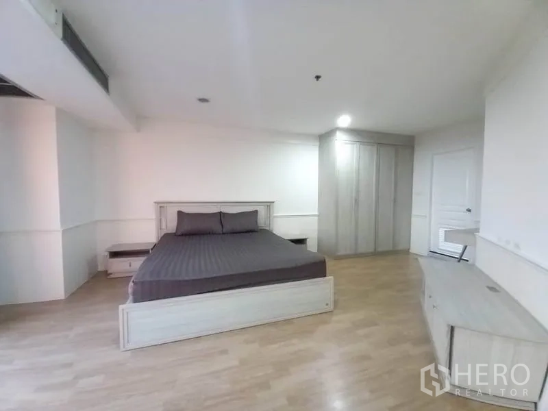 Condominium for rent in Khlong Toei, Bangkok - Master bedroom angle showing large wardrobe, dresser, and light wood furnishings.