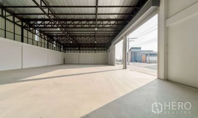 Warehouse for rent in Bang Bo, Samut Prakan - Spacious warehouse bay with high steel truss roof and a wide roller door opening to the street.