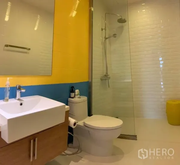 Condominium for rent in Phaya Thai, Bangkok - Modern bathroom with glass-enclosed rain shower, yellow and blue accent tiles, and vanity.