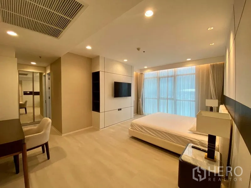 Condominium for rent in Khlong Luang, Pathum Thani - Spacious bedroom with desk, wall-mounted TV, built-in storage and full-height windows.