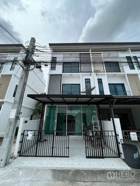 Townhouse for sale in Bang Kapi, Bangkok - Three-storey modern townhouse facade with gated carport and balcony.