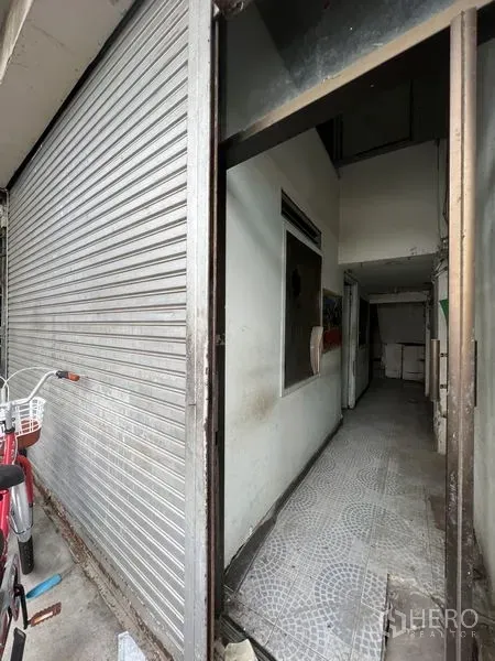 Shophouse for rent in Watthana, Bangkok - Ground-floor shophouse entrance with metal roller shutter and a narrow tiled corridor in Watthana, Bangkok.