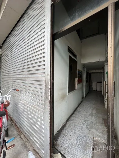Shophouse for rent in Watthana, Bangkok - Ground-floor shophouse entrance with metal roller shutter and a narrow tiled corridor in Watthana, Bangkok.