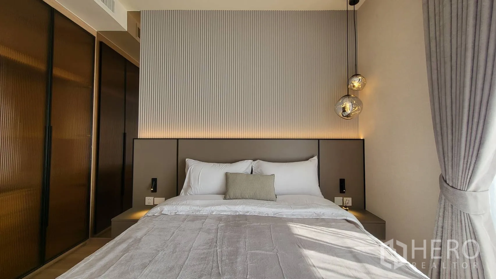 คอนโด for sale in Watthana, Bangkok - ห้องนอนหลักพร้อมเตียงใหญ่ ผนังหัวเตียงลอน ไฟแขวน ตู้เสื้อผ้าบานเลื่อน และหน้าต่างเต็มผนัง