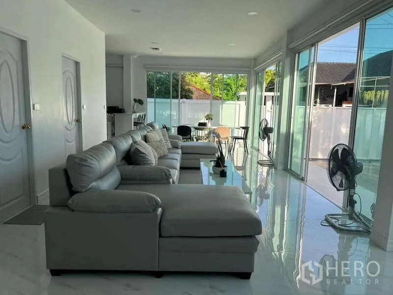 Detached House for rent in Lat Krabang, Bangkok - Open‑plan living room with long sectional sofa and full‑height sliding glass doors.
