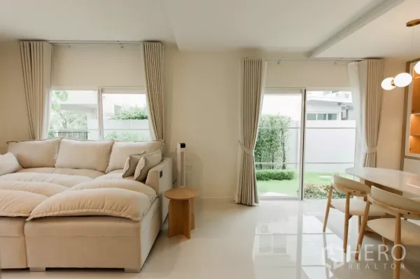 บ้าน ให้เช่าหรือขายในBang Phli, Samut Prakan - ห้องนั่งเล่นสว่างด้วยโซฟาขนาดใหญ่และประตูกระจกบานเลื่อนเปิดสู่สวน