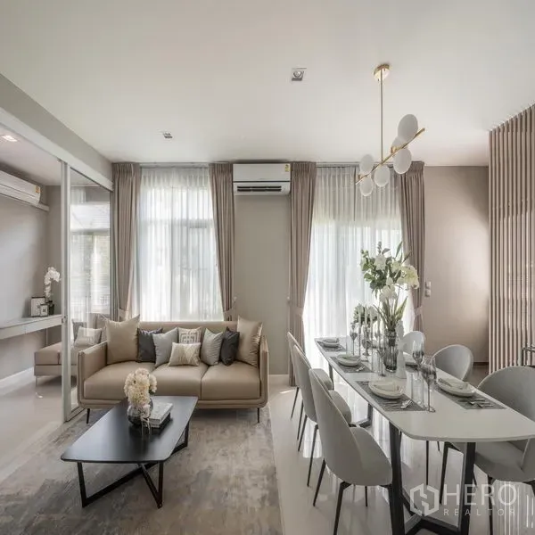 Detached House for rent in Samut Prakan - Bright open-plan living and dining room with sofa, curtains and a modern chandelier.