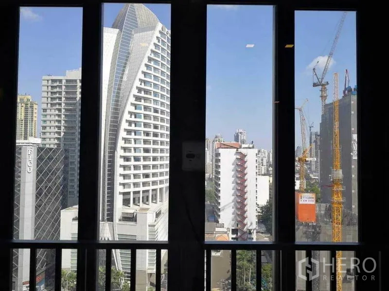 Condominium for rent in Watthana, Bangkok - City skyline view of the Asok area seen through tall windows and a balcony railing.