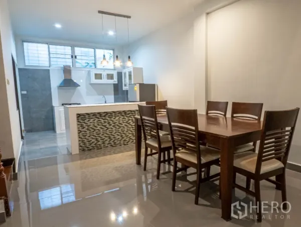 Townhouse for rent in Khlong Toei, Bangkok - Open-plan dining area with a six-seat wooden table beside a modern kitchen island and pendant lights.