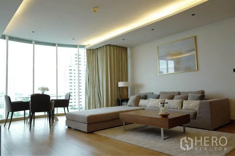 Condominium for rent or sale in Phaya Thai, Bangkok - Light-filled living room with L-shaped sofa, coffee table and curved panoramic windows.