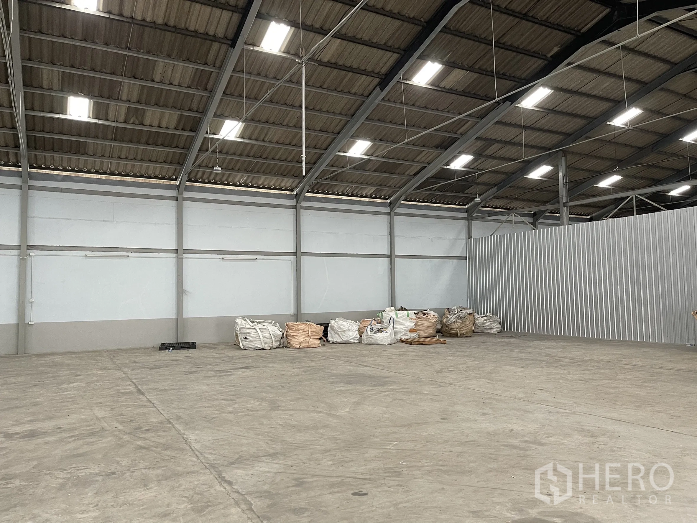 Factory for rent in Mueang Samut Prakan, Samut Prakan - Factory area with corrugated partition wall and stacked material bags.