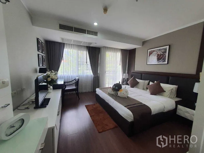 房间 出租在Watthana, Bangkok - 卧室设大窗与遮光窗帘，电视柜，可见室外绿意。