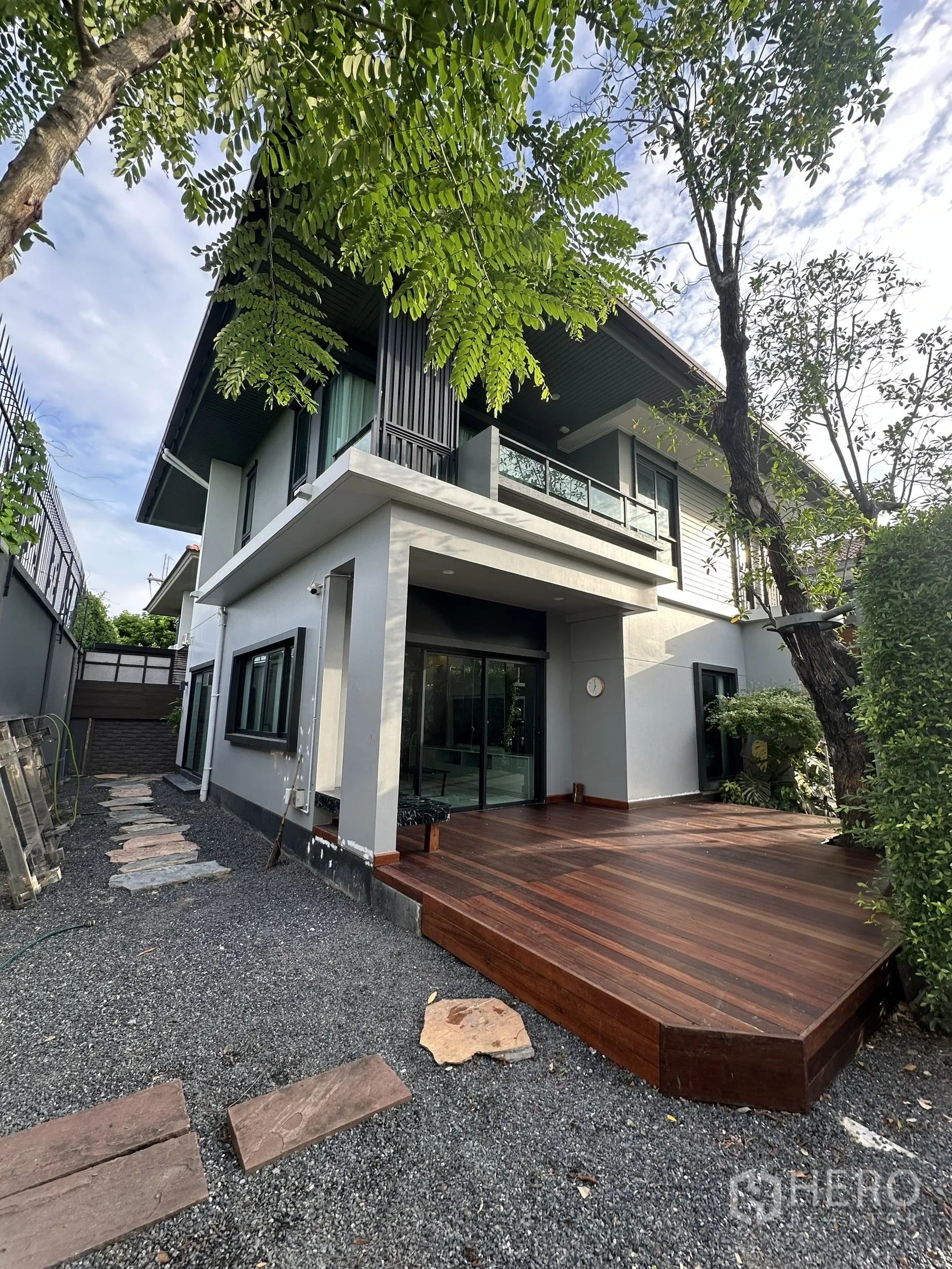 Detached House for rent or sale in Lam Luk Ka, Pathum Thani - Outdoor wooden deck terrace beside the house with sliding glass doors and greenery.