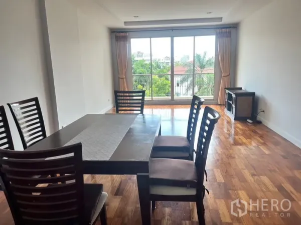 Condominium for rent in Sathon, Bangkok - Dining area with wooden floors and floor-to-ceiling sliding doors opening to leafy views at Baan Nunthasiri in Sathon, Bangkok.