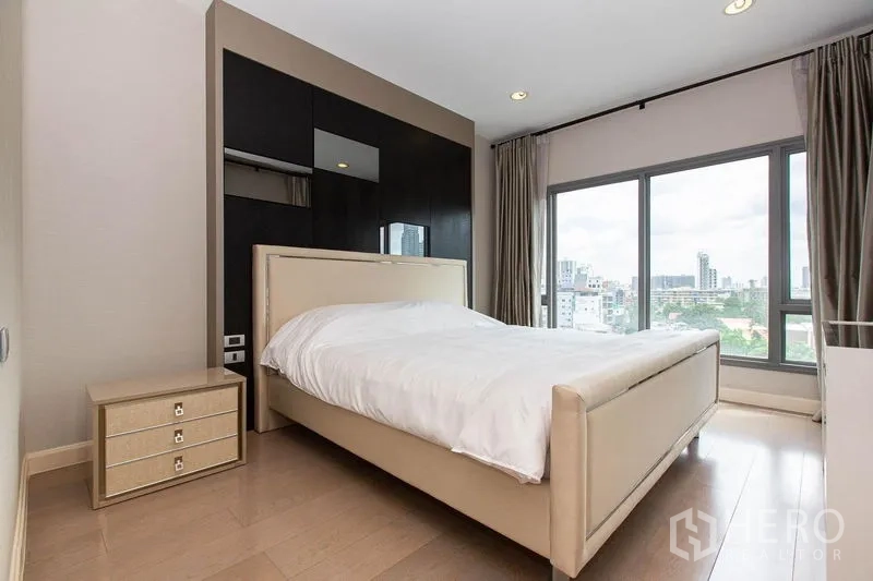 公寓 出租在Khlong Toei, Bangkok - 主卧配软包床与床头柜，转角大窗可欣赏城市景观。