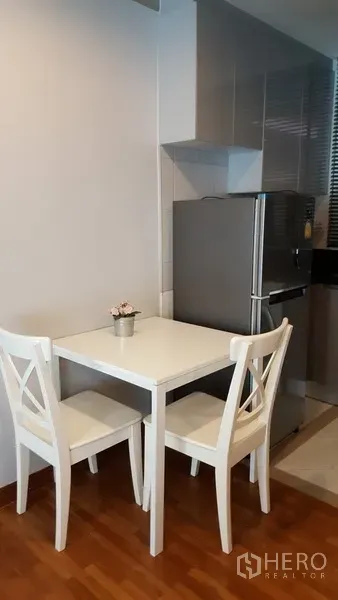 Condominium for rent in Watthana, Bangkok - Small dining nook with a white table and two chairs beside the kitchen on warm wooden flooring.