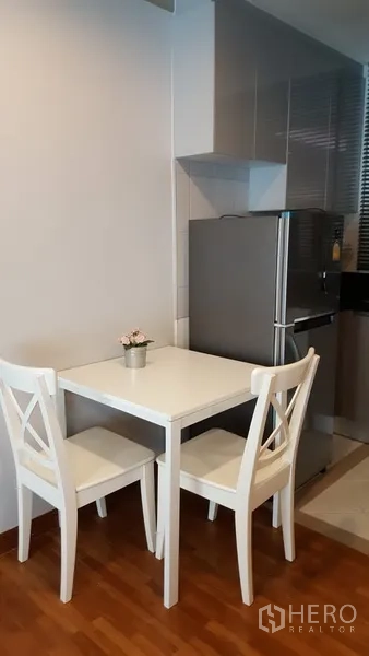Condominium for rent in Watthana, Bangkok - Small dining nook with a white table and two chairs beside the kitchen on warm wooden flooring.