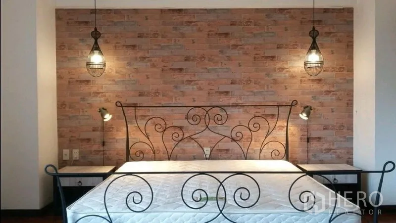 Condominium for rent in Khlong Toei, Bangkok - Bedroom with wrought-iron bed frame, exposed brick accent wall, pendant lights and twin bedside tables.