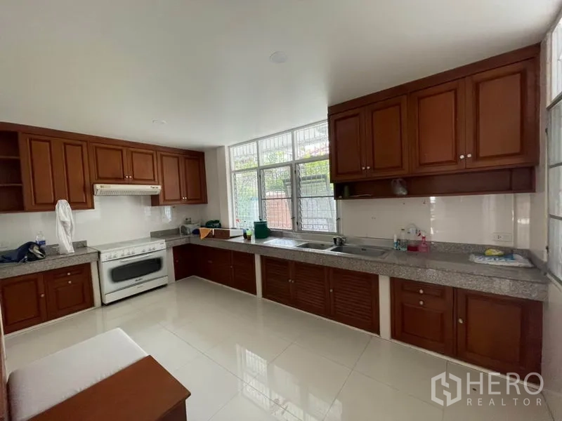 Detached House for rent in Khlong Toei, Bangkok - Closed kitchen with long granite countertops, wooden cabinets, oven and large window.