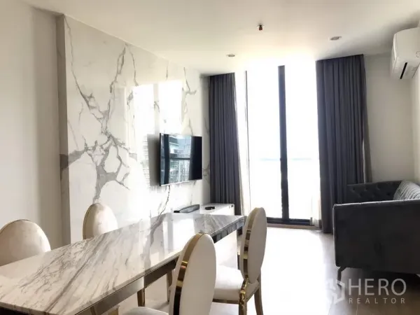 公寓 出租或出售在Watthana, Bangkok - 明亮的客餐厅，石纹背景墙、壁挂电视、大理石餐桌、灰色沙发与落地窗。