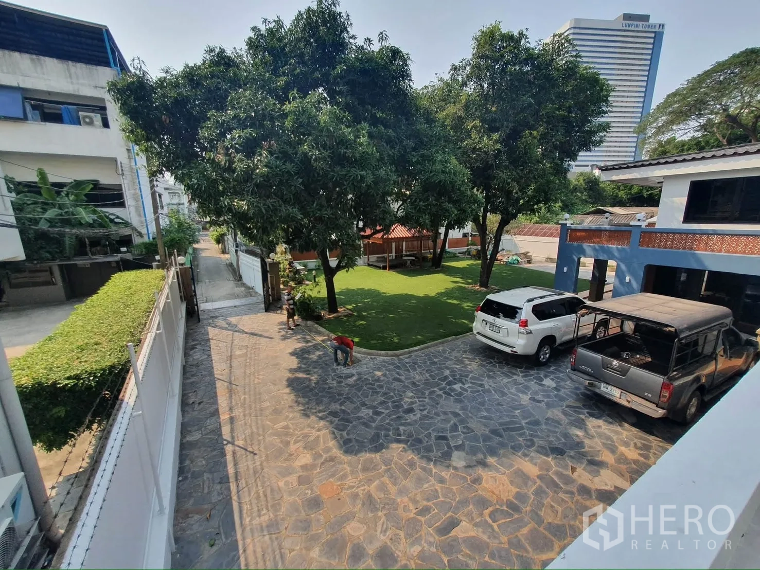 独栋房屋 for rent in Sathon, Bangkok - 石材铺面的车道，带大门与树荫，旁有多辆车停放在草坪边。