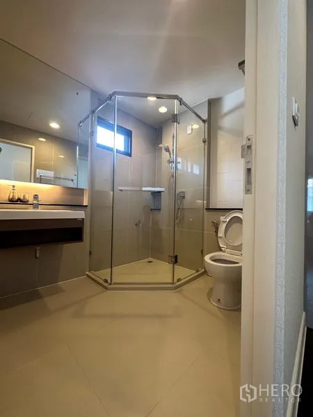 Detached House for rent or sale in Lam Luk Ka, Pathum Thani - Bathroom with glass-enclosed shower, vanity and toilet in neutral tiles.
