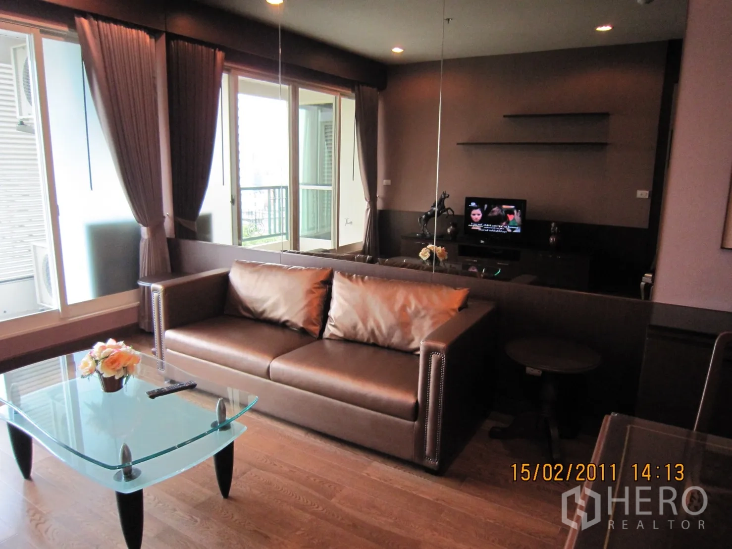 Condominium for rent or sale in Pathum Wan, Bangkok - Modern living room with brown leather sofa, glass coffee table, TV console, and balcony doors with curtains.