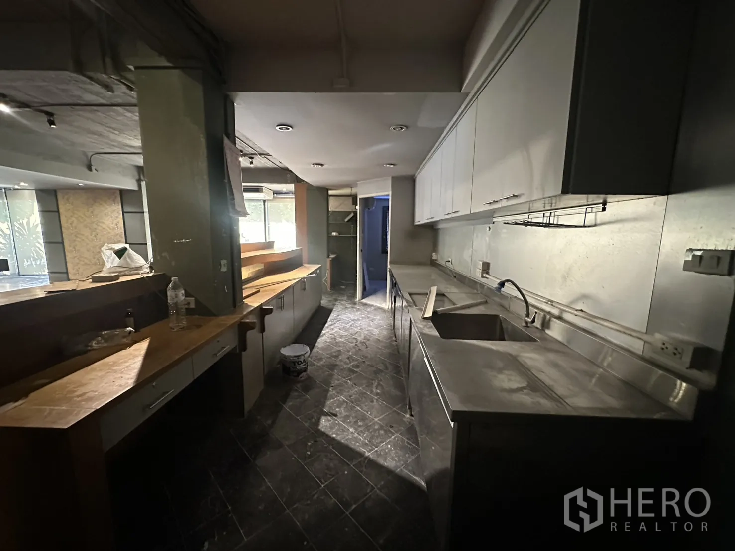 Retail Space for rent in Watthana, Bangkok - Back‑of‑house prep kitchen with stainless counters, sink, overhead cabinets, and dark tiled floor.