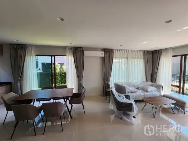Detached House for rent in Bang Kapi, Bangkok - Open-plan living and dining area with large windows, curtains, table and sofa.