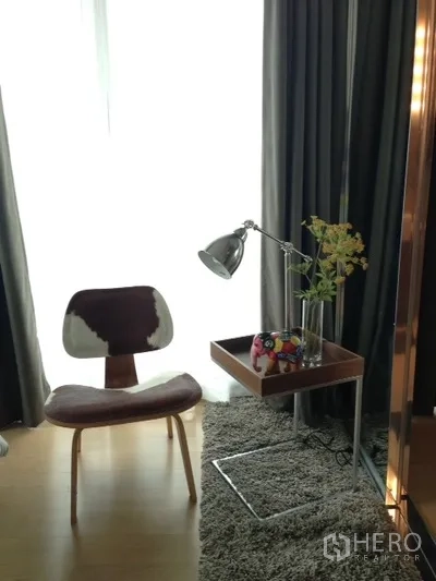 Condominium for rent in Phaya Thai, Bangkok - Reading corner by full-height window with modern chair, side table, desk lamp and rug.