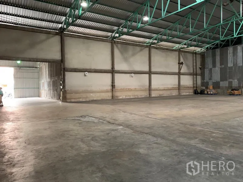Warehouse for rent in Mueang Pathum Thani, Pathum Thani - Open-plan warehouse hall with bright lighting, smooth concrete slab and a large roller door for easy access.