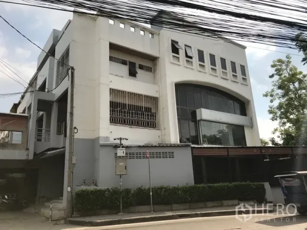 Home Office for rent in Phra Khanong, Bangkok - Multi-storey white home office building with large arched glass frontage, gated parking and hedge along a quiet street.