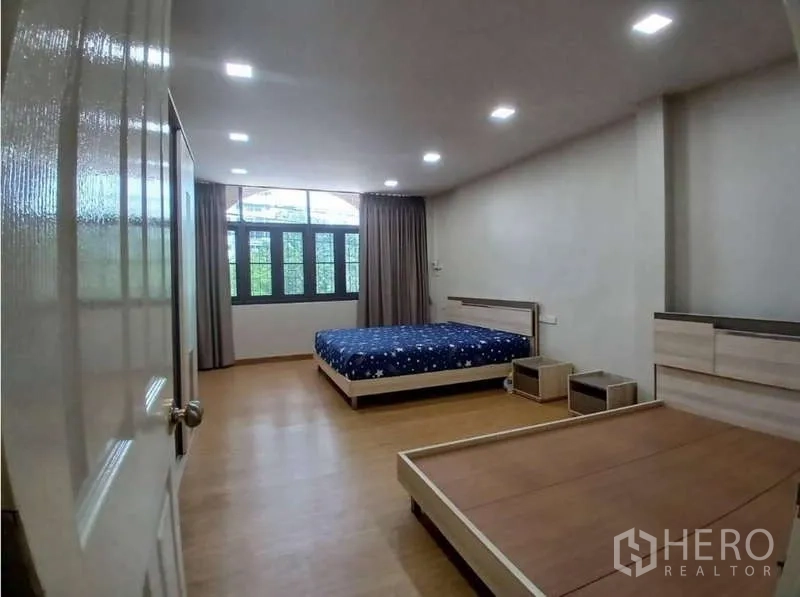 Shophouse for rent in Phra Khanong, Bangkok - Spacious bedroom with wood flooring, large windows and curtains, furnished with bed and side tables.