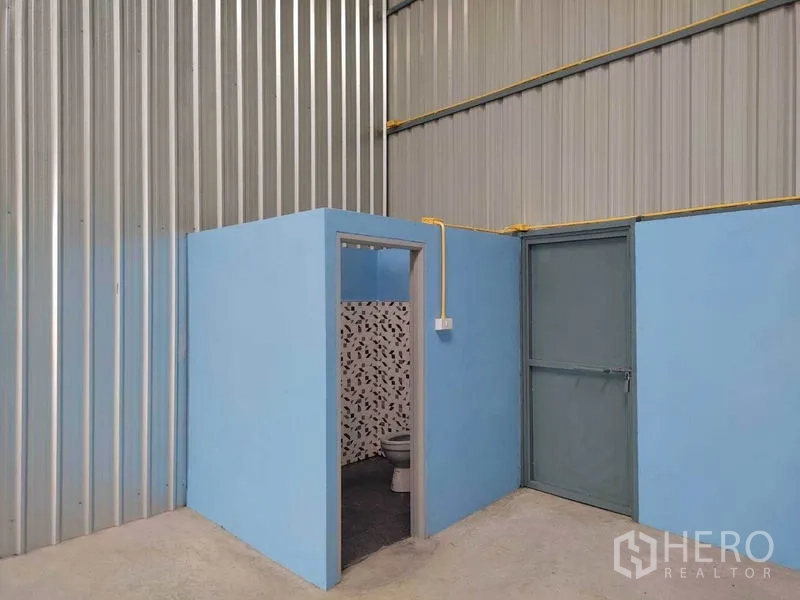Warehouse for rent in Bang Yai, Nonthaburi - Built-in restroom and side door inside the warehouse with blue partition walls and tiled bathroom.